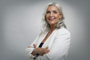 Studio shot of grey haired senior woman wearing elegant clothes while standing at isolated grey background. Copy space.