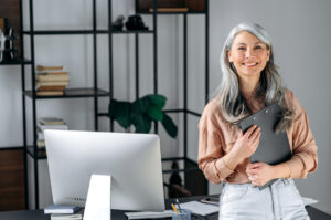 Portrait of a confident beautiful smart gray-haired asian business woman or manager, standing in modern office, dressed in stylish clothes, holding folder in hands, looking at camera, smiling friendly