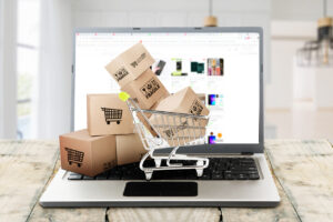 Close up of online shopping app on the laptop with trolley full of packages over wooden table
