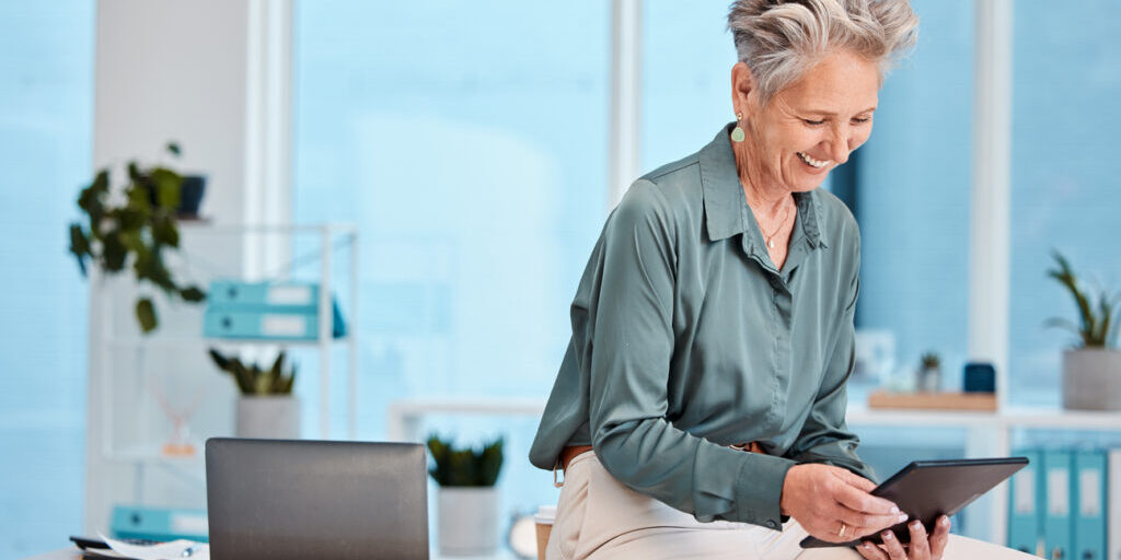 Senior, business woman and tablet in office for social media, internet browsing or research. Happy, elderly and female employee from Canada with digital touchscreen for networking or web scrolling.